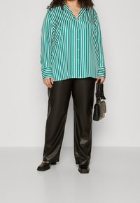 Chemise à manches longues rayée verte et blanche avec col, associée à un pantalon en similicuir noir et un petit sac à main noir.