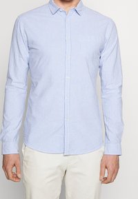 Gestreiftes Hemd in Hellblau und Weiß. Lange Ärmel, Kragen, Brusttasche und ein strukturiertes Baumwollmaterial. Klassische Passform.