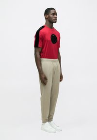 Piros póló fekete bársony vállcsíkkal és kör alakú logóval, bézs melegítőnadrággal és fehér tornacipővel párosítva. Egyszerű dizájn és laza szabás.