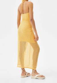 Gul virkad maxikjol med öppen vävsmönster, halterneck och hög slits. Matchad med beige plattformssandaler med korsade remmar.