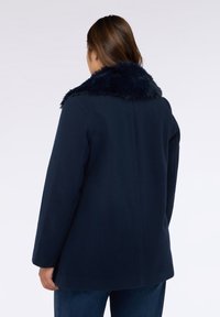 Marineblauer Mantel mit einem Kragen aus Kunstfell, mit geradem Schnitt und langen Ärmeln. Glatte Textur des Stoffes mit sauberer Silhouette.