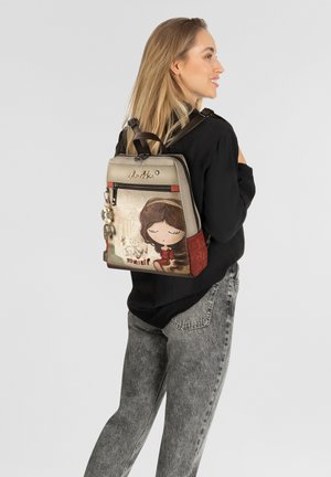 Rucksack mit einer strukturierten, cremefarbenen Vorderseite, die eine Cartoon-Mädchen-Grafik zeigt. Braune Träger und bunte Anhänger verleihen Details und Funktionalität.