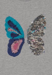 Šedé tričko z látky s designem motýla vyrobeným z barevných flitrů v odstínech modré, růžové a stříbrné, s lesklou texturou.