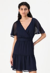 Μπλε ναυτικού κοντό φόρεμα σε ελαφρύ ύφασμα, με V λαιμόκοψη, φτερωτά μανίκια, στενή μέση και τιράντες με ρίγες.
