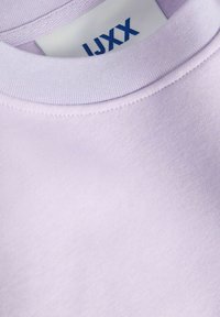 Lavender sweatshirt featuring a ribbed crew neck, soft texture, and a label with blue text. Seam detailing around the neckline.