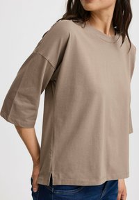 Lys brun kortærmet t-shirt lavet af blødt stof, med en afslappet pasform og sidespidser ved kanten for ekstra komfort.