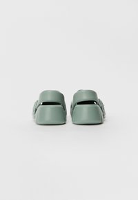 Grønne gummislipper med to brede stropper og åpen hældesign. Teksturert overflate, rund tå og minimalistic stil.