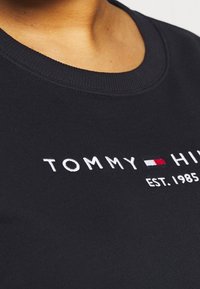 Felpa nera con collo rotondo, caratterizzata da testo ricamato bianco "TOMMY HILFIGER EST. 1985" e un piccolo accento logo rosso e bianco.