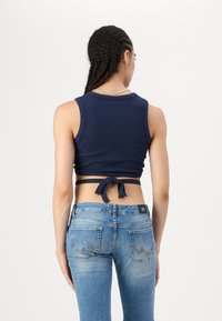 Tengerészkék bordázott crop top, hátsó megkötő részlettel, világoskék, szűkített farmernadrággal párosítva, hímzett hátsó zsebekkel.