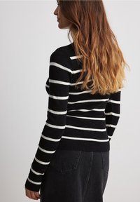Zwart-wit gestreepte gebreide trui met lange mouwen, geribde manchetten en een aansluitend ontwerp, gecombineerd met high-waisted zwarte denim.