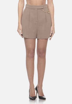 Shorts beige a vita alta su misura con pieghe frontali e piccolo dettaglio a catena dorata, indossati con scarpe nere con tacchi alti.