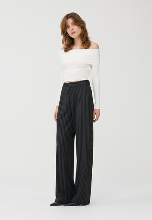 Top bianco a spalle scoperte in maglia abbinato a pantaloni larghi a righe nere con vita alta, caratterizzati da un dettaglio con bottone frontale.