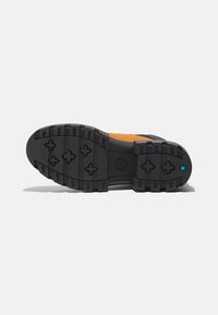 Schwarze Gummisohle mit tiefem Profil und blauen Akzenten, entwickelt für Griffigkeit. Der Schuh hat ein kontrastierendes oranges Obermaterial.