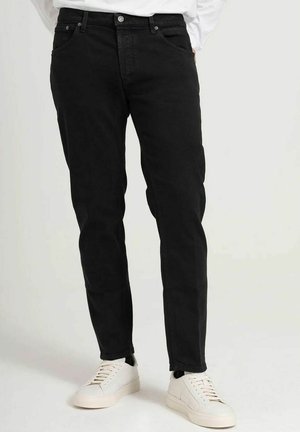 Sorte denimjeans med en slim fit, fem lomme-design og en let indsnævring. Båret med hvide sneakers, der har minimalistiske detaljer.