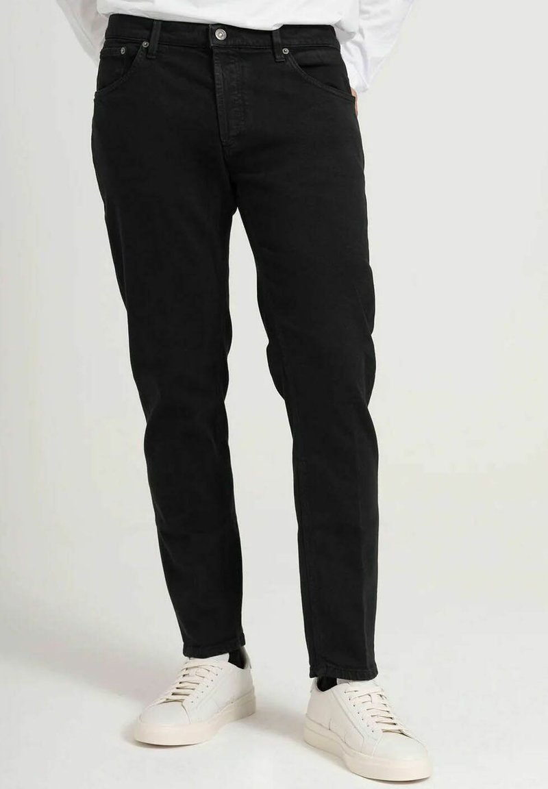 Zwarte spijkerbroek van denim met een slim fit, vijf zakken en een lichte taper. Draagt een witte sneakers met minimalistische accenten.