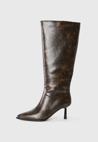 Brun sliten läder knähöga stövel med spetsig tå och tunn stiletto-klack mot en vit bakgrund.