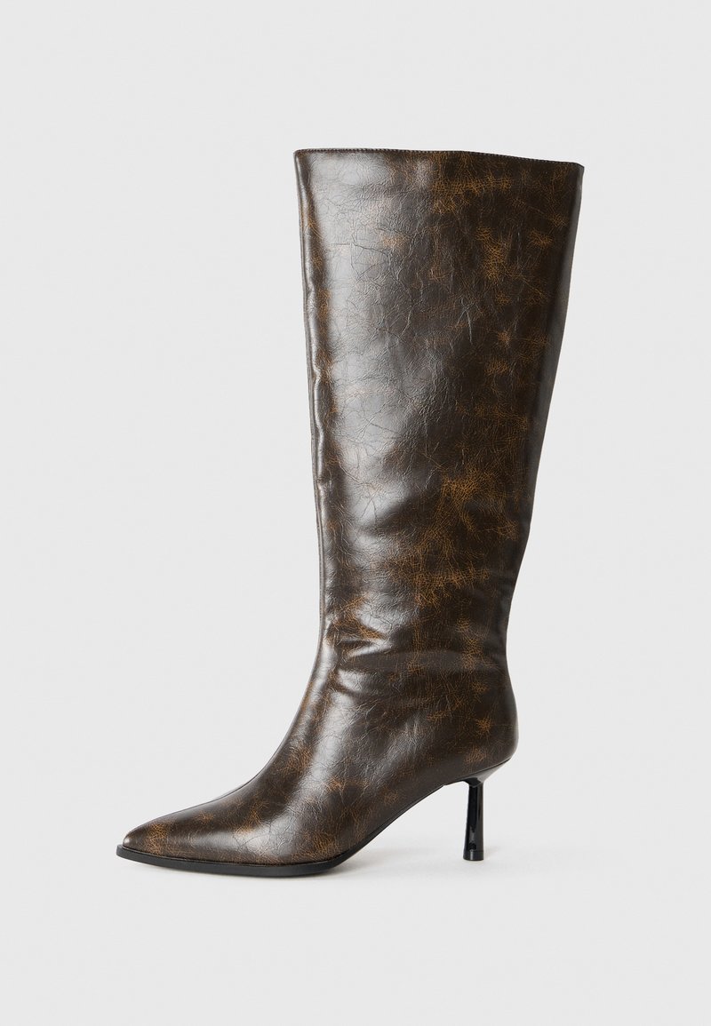 Brun sliten läder knähöga stövel med spetsig tå och tunn stiletto-klack mot en vit bakgrund.