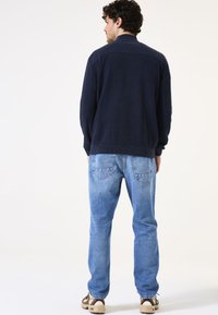 Suéter texturizado color navy con diseño de canalé, combinado con jeans rectos de un azul claro y zapatos de tonos neutros. Vista trasera, detalle mínimo.