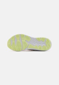 Semelle de chaussure présentant une base blanche flexible avec des grips en caoutchouc jaune-vert texturé et un motif ondulé pour une meilleure traction.