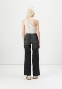 Asymmetrical beige top, high-waisted dark denim jeans, wide legs, and platform sandals with metallic accents; smooth texture, minimal design.