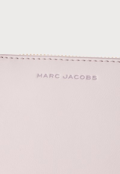 Крупен план на бледо розов кожен артикул Marc Jacobs с релефно лого на марката и видими шевове близо до златист цип.