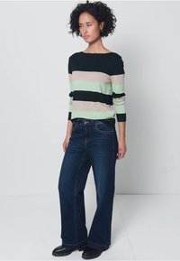 Gestreifter Pullover in Dunkelgrün, Beige und Mint, kombiniert mit dunkelblauen weitgeschnittenen Jeans. Der Pullover hat lange Ärmel und einen Rundhalsausschnitt.
