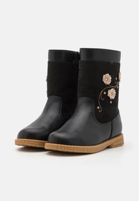 Czarne botki do kostki z brązowymi gumowymi podeszwami, z różowymi haftowanymi i aplikowanymi kwiatami po zewnętrznej stronie każdej botki.