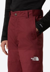 Pantaloni outdoor bordo cu o cămașă neagră texturată cu mâneci lungi. Brand vizibil pe picior și închidere cu nasture la talie. Material durabil.
