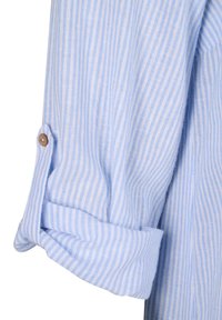 Himmelblau gestreifte Baumwollhemdärmel mit umgeschlagenem Saum, Details aus Holzknöpfen und weicher Textur. Die Streifen wechseln sich zwischen hellblau und dunkelblau ab.