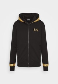 Svart zip-up hoodie med en guldlogotyp, kontrasterande gula detaljer på huvan och ärmsluten, med en slät yta och långa ärmar.