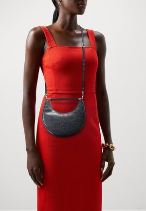 Borsa in pelle nera con motivo a coccodrillo dalla forma curva, dotata di tracolla nera staccabile, indossata sopra un vestito rosso.