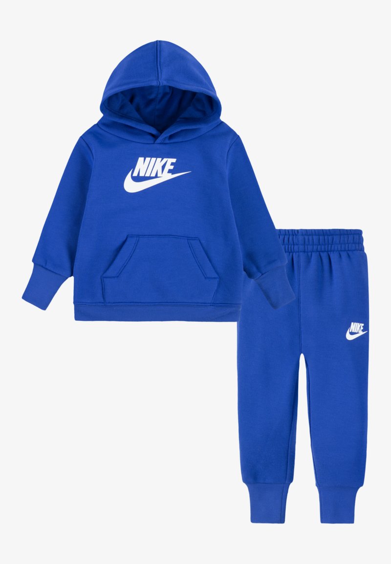 Zila Nike kapuce ar priekšējo kabatu un balto logotipu, kopā ar atbilstošām zilām sporta biksēm ar elastīgu jostu un logotipu.