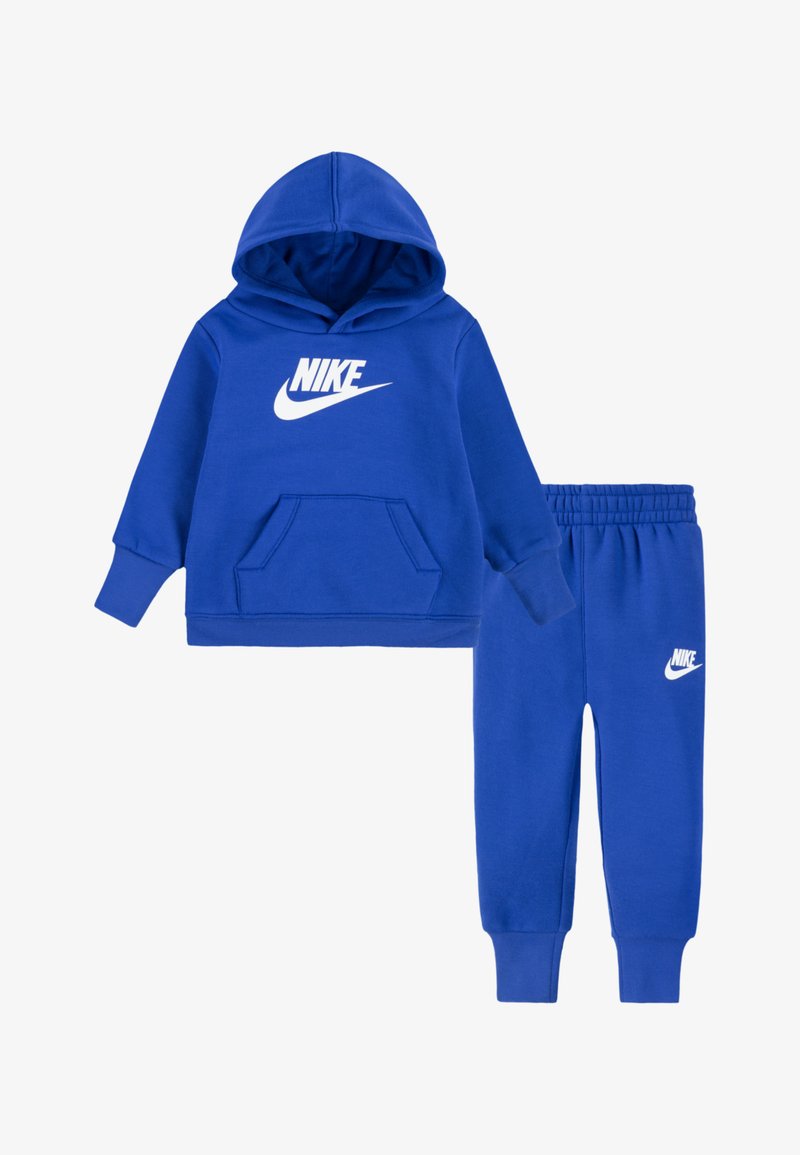 Zila Nike kapuce ar priekšējo kabatu un balto logotipu, kopā ar atbilstošām zilām sporta biksēm ar elastīgu jostu un logotipu.