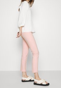 Vit långärmad blus, rosa tight byxor och svarta sandaler med vita korskorsade remmar. Släta tyger och skräddarsytt passform.