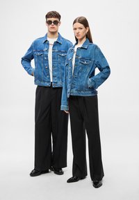 Közép kék farmerdzsekik klasszikus zsebekkel és gombokkal, széles fekete nadrággal és fekete cipővel párosítva. Mindkét szett fehér felsőket tartalmaz.