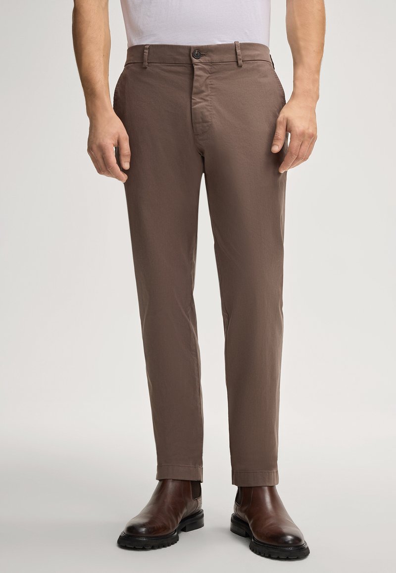 Pantaloni in cotone marrone misto con vestibilità slim, dotati di chiusura a bottone, passanti per la cintura e una texture liscia, abbinati a stivali marroni scuri.