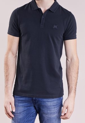 Czarna koszulka polo z klasycznym kołnierzykiem, krótkimi rękawami i małą naszywką z logo marki na klatce piersiowej. Miękki, gładki materiał z dopasowanym krojem.