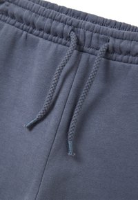 Graue Baumwoll-Jogginghosen mit elastischem Bund und verstellbarem Kordelzug aus geflochtenem Material. Glatte Textur mit subtiler Helligkeit.