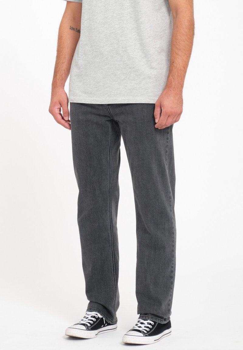Jeans de mezclilla gris con un corte recto, presentan un acabado desgastado y un diseño básico de cinco bolsillos, combinados con zapatillas negras.