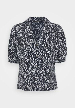 Blouse bleu marine à manches courtes avec des pois blancs irréguliers, boutonnière devant et col cranté.