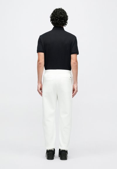 Čierne polokošeľa, biele tepláky s elastickým pásom a čierne tenisky. Pohľad zozadu ukazuje jednoduchý dizajn a hladkú štruktúru látky.