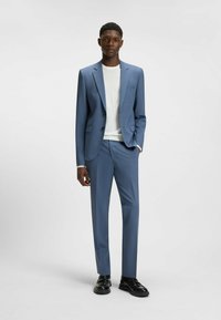 Complete blu chiaro, taglio slim, giacca monopetto con rever a punta, pantaloni abbinati, indossata sopra una maglietta bianca a girocollo, abbinata a scarpe nere.