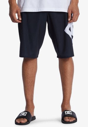 Shorts de sport noirs avec un logo géométrique blanc sur le côté gauche, dotés d'une taille élastique et d'un tissu léger. Sandales noires à glisser.