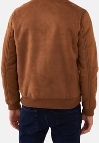 Brown suede bomber jacket with ribbed cuffs and hem, smooth texture, and a minimalistic design. Features subtle stitching details.