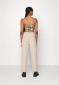 Pantalons larges beiges avec une texture lisse, dotés de poches arrière et d'une étiquette. Le haut est un bandeau court à carreaux verts. Bottines noires à la cheville.