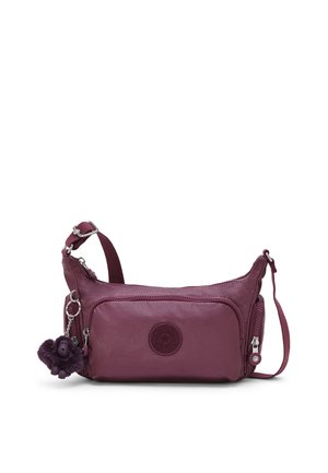 Petit sac bandoulière violet foncé avec sangle réglable, poche zippée à l'avant et un porte-clés singe duveteux attaché.