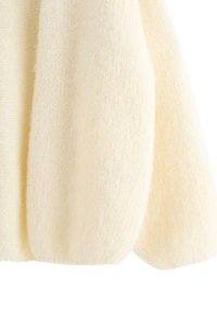 Kremfarvet blødt strikket stof med en let luftig tekstur, der viser en afrundet ærmedetalje.