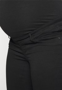 Pantalones de maternidad negros con una cinturilla elástica, diseñados para la comodidad. La tela es suave, con una forma ajustada y un detalle de costura mínimo.