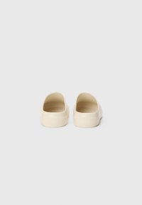 Beige slip-on clogs with smooth plastic material, wide openings, and a textured insole. Flat base and subtle curves, minimalist design.