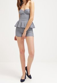 Top peplum in stampa a quadretti con design senza spalline, abbinato a pantaloni corti coordinati. Di colore blu navy con texture liscia; indossato con tacchi alti blu navy.